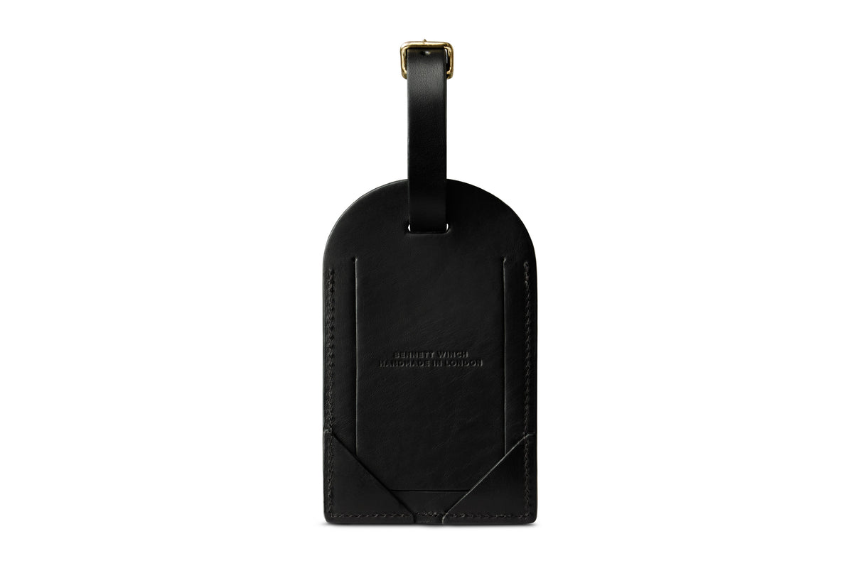 Back of a black leather luggage tag with close ID card flap and connecting strap with buckle.