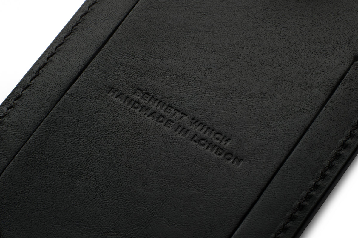 Close-up of "Bennett Winch" and "Handmade in London" embossed on the back of a black leather luggage tag.