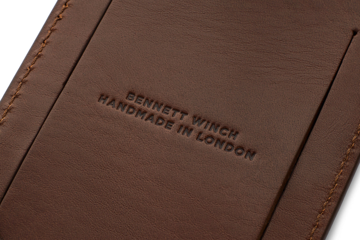 Close-up of the back of a brown luggage tag, "Bennett Winch" and "Handmade in London" embossed in the center.
