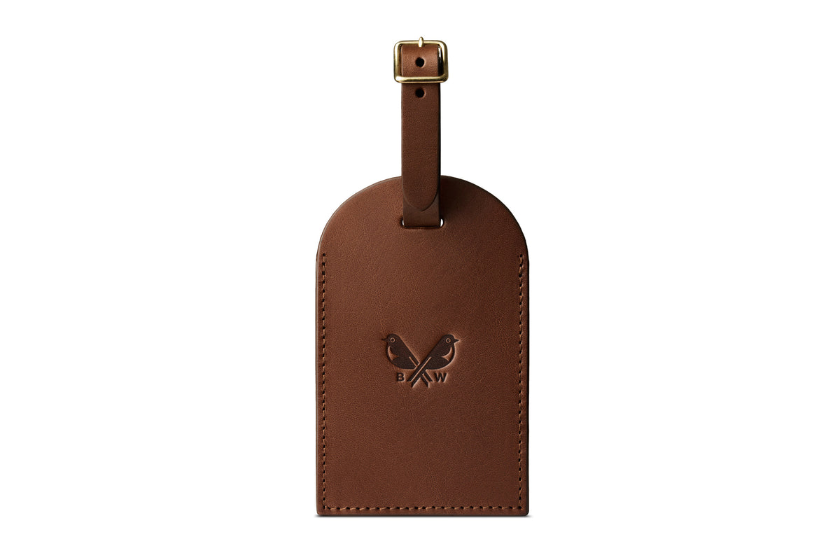 Front of a brown leather luggage tag with embossed Bennett Winch logo and brass buckle fastener.