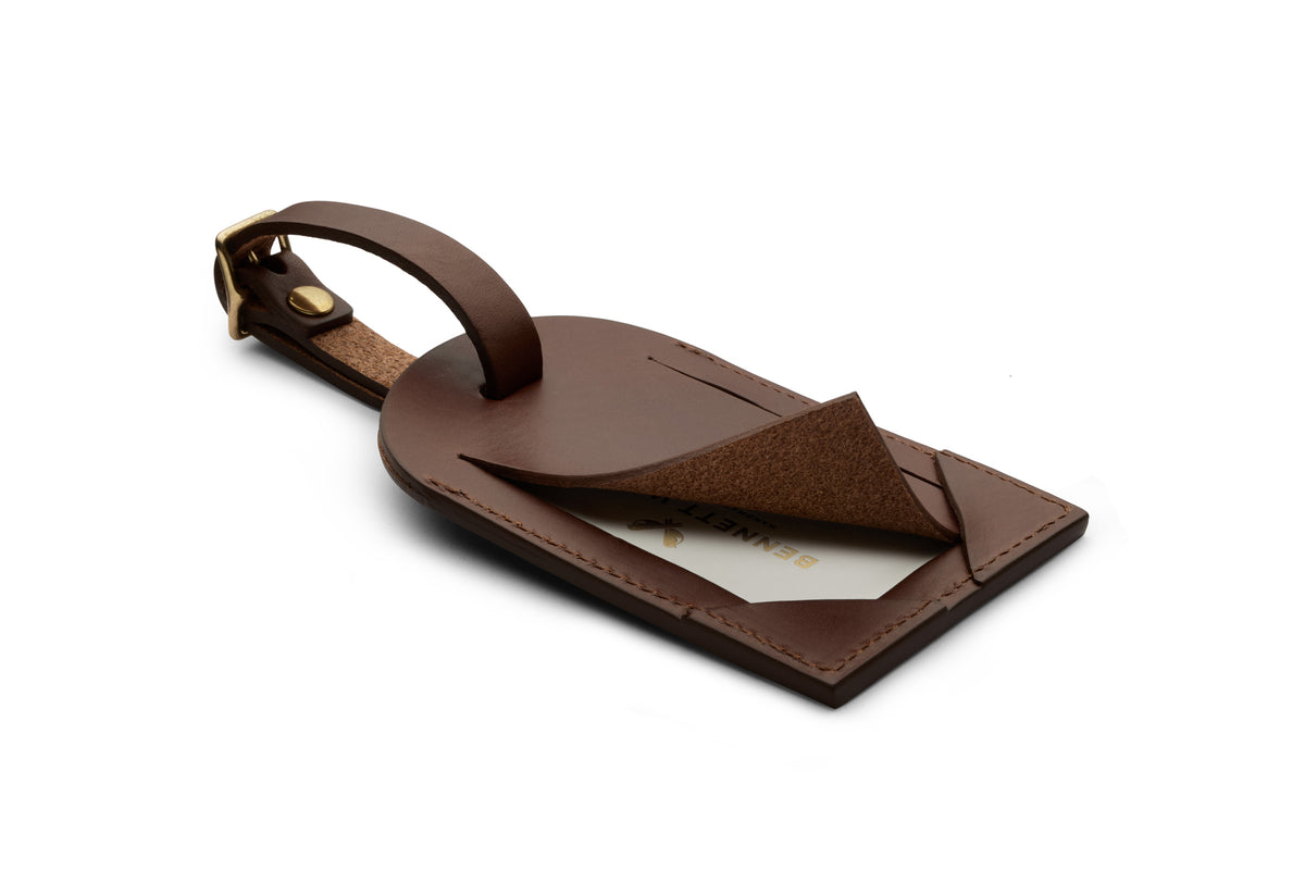 Back of a brown leather luggage tag with business card flap opening and brass buckle fastener on strap.
